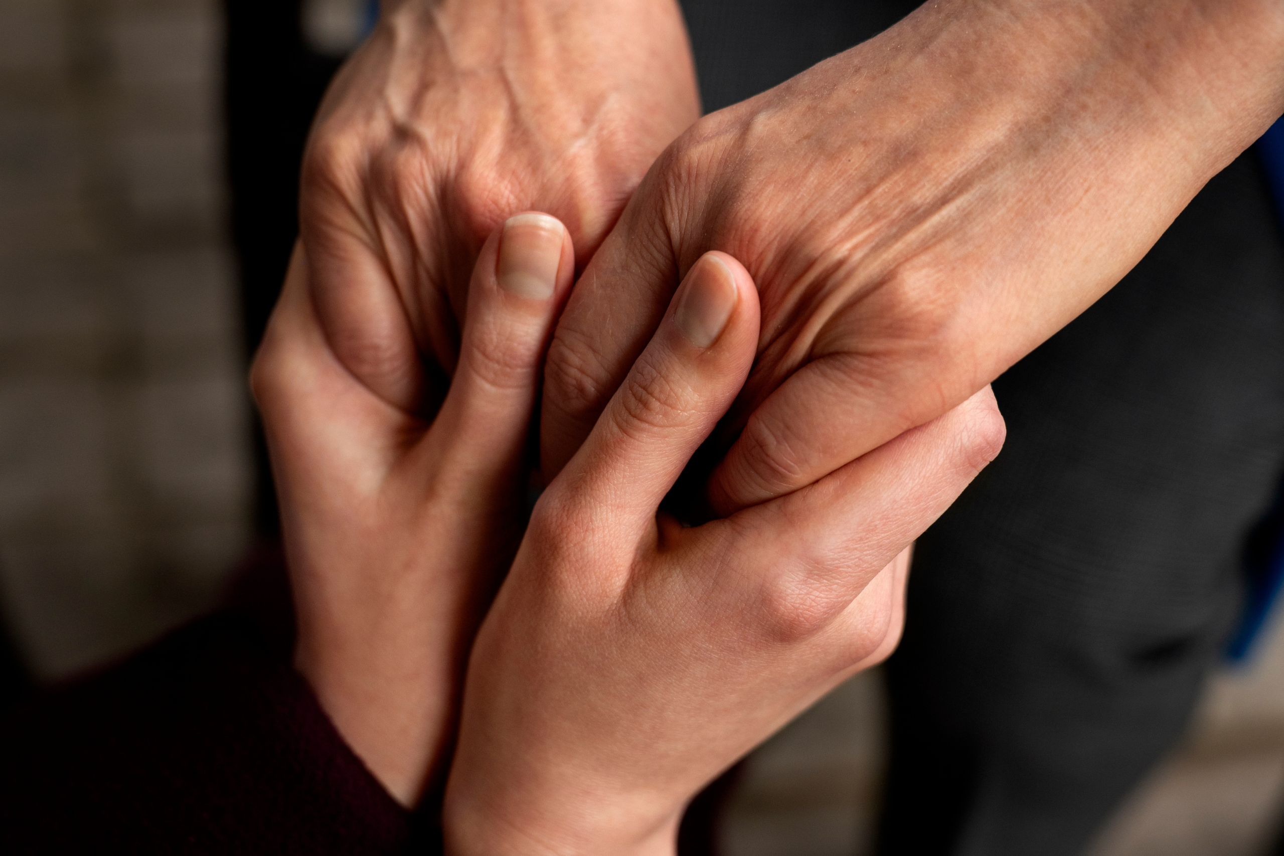 Ein junges Paar Hände hält ein älteres Paar Hände fest. Der Hintergrund ist verschwommen.